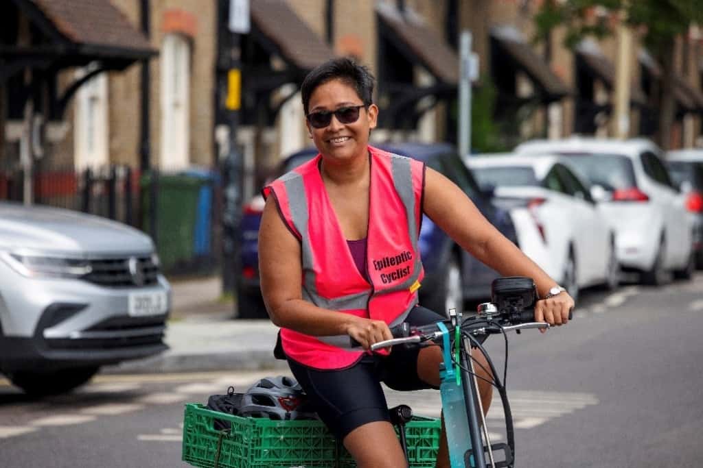 Quailyn cycling towards the camera smiling, on her bright pink vest are the words 'Epileptic cyclist'