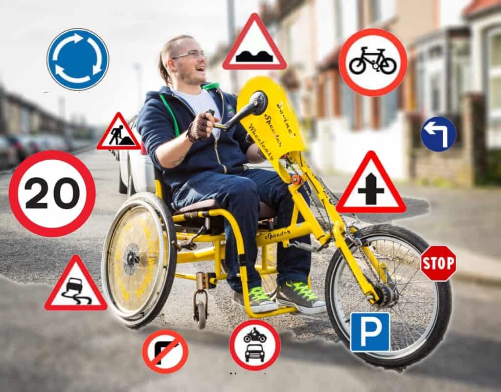 A smiling guy sits on a handcycle while road signs float around him.