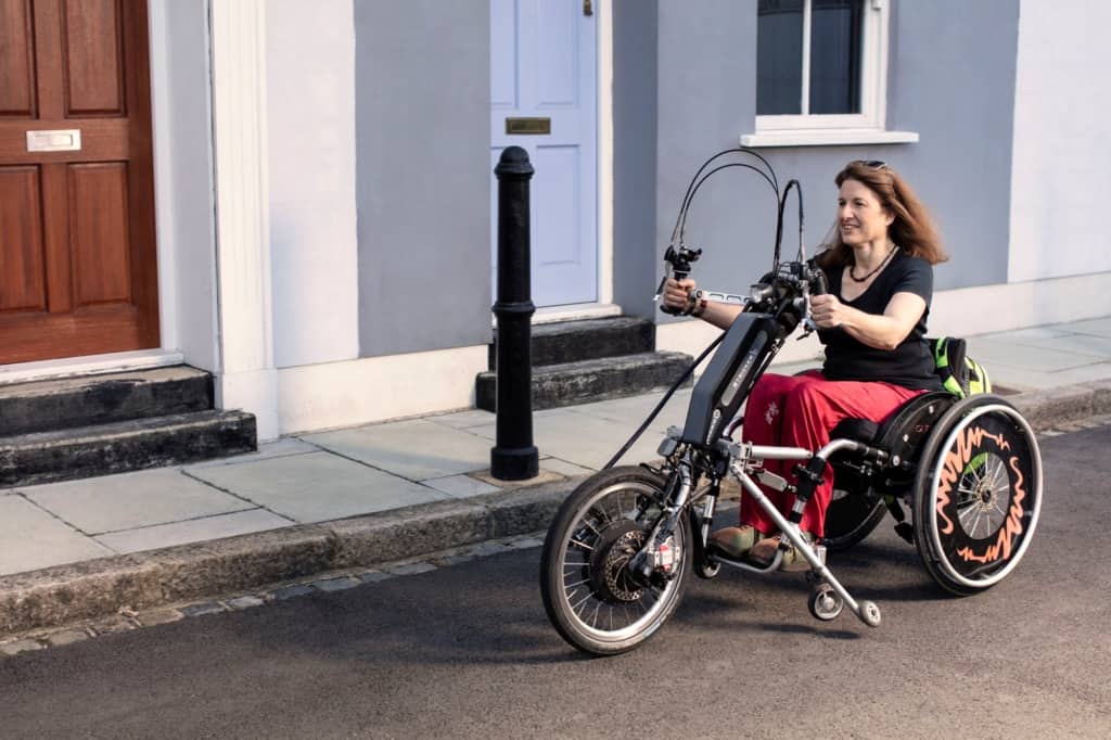 A woman smiles while riding her handcycle, the wind blowing her hair shows she's in motion.