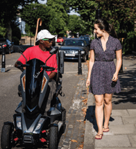 Image from CWIS2 Report. A man rides a mobility scooter on a residential road, talking to a women walking on the pavement.