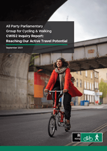 Front cover of All Part Parliamentary Group for Cycling & Walking CWIS2 Inquiry Report. A woman wearing an orange coat cycles a red Brompton bike on a quiet urban road.