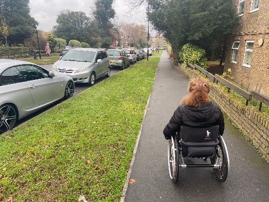 A good quality pavement, short cropped grass on the verge on the left, in front of us a wheelchair user travels along it. 