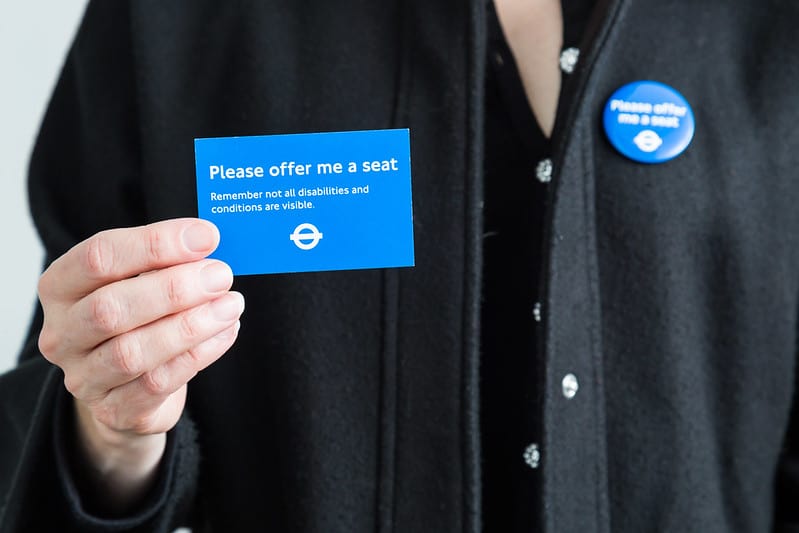 A person holding a 'Please offer me a seat card'.