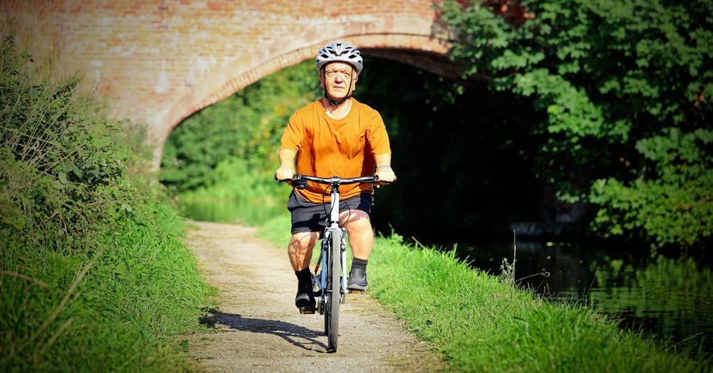 A person with disproportionate dwarfism riding a bicycle on a path next to a canal