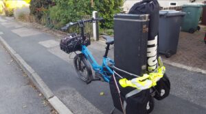 A cargo cycle on a pavement with bags full of very tall items on the back