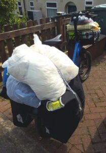 Photo shows rear of a cargo cycle loaded with large bulging white and blue plastic bags