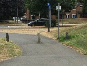 Photo of shared-use cycle path surfaced with grey asphalt. In the middle of the path is a grey concrete bollard approx 60cm high.