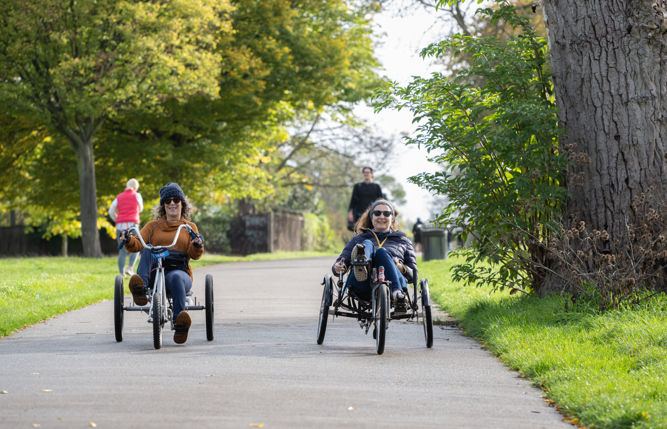 Two women cycling through a park on recumbent trikes