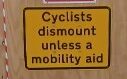 Photo of a temporary sign, black writing on yellow background reads "cyclists dismount unless a mobility aid"