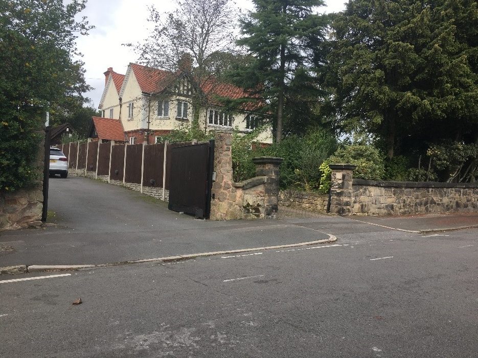 Two driveways into large detached houses. One has a dropped kerb leading over a continuous pavement. One has kerbs giving a continuous carriageway and deprioritised pavement.