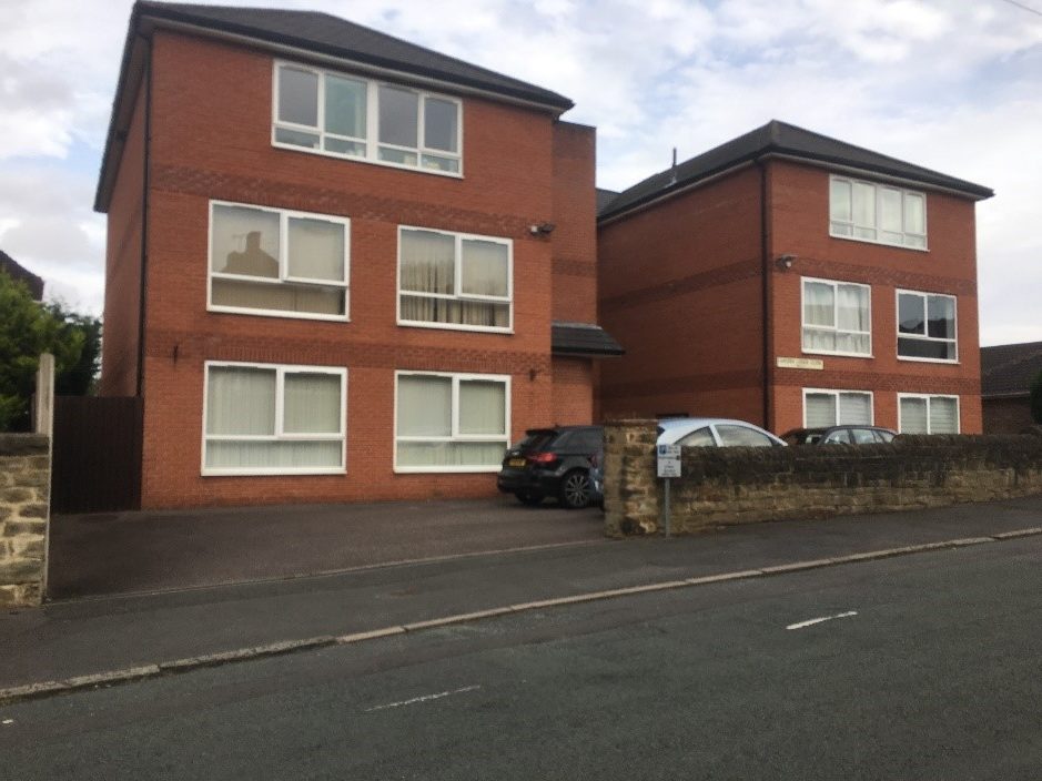 A block of low-rise flats with dropped kerb entrance over continuous pavement into car park.