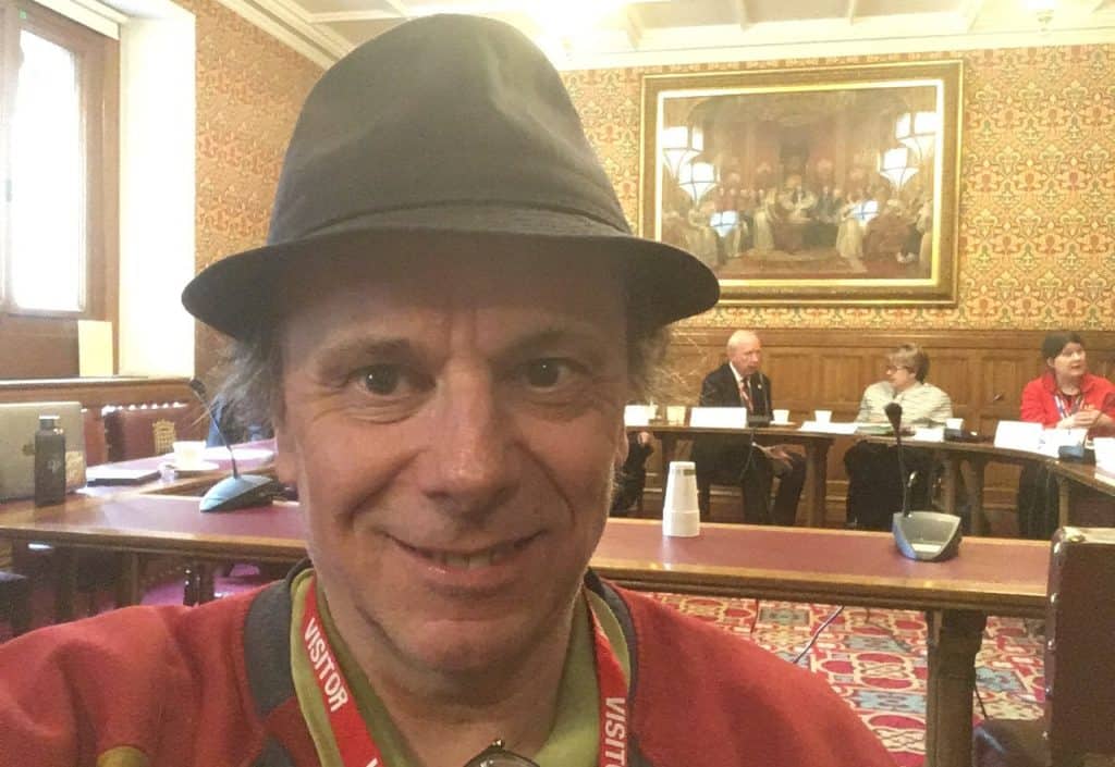 Selfie of Ben in a formal political consultation. He is wearing a red jumper and his customary trilby. Behind him are key political figures lined behind a desk.