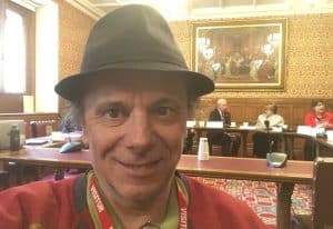 Selfie of Ben in a formal political consultation. He is wearing a red jumper and his customary trilby. Behind him are key political figures lined behind a desk.