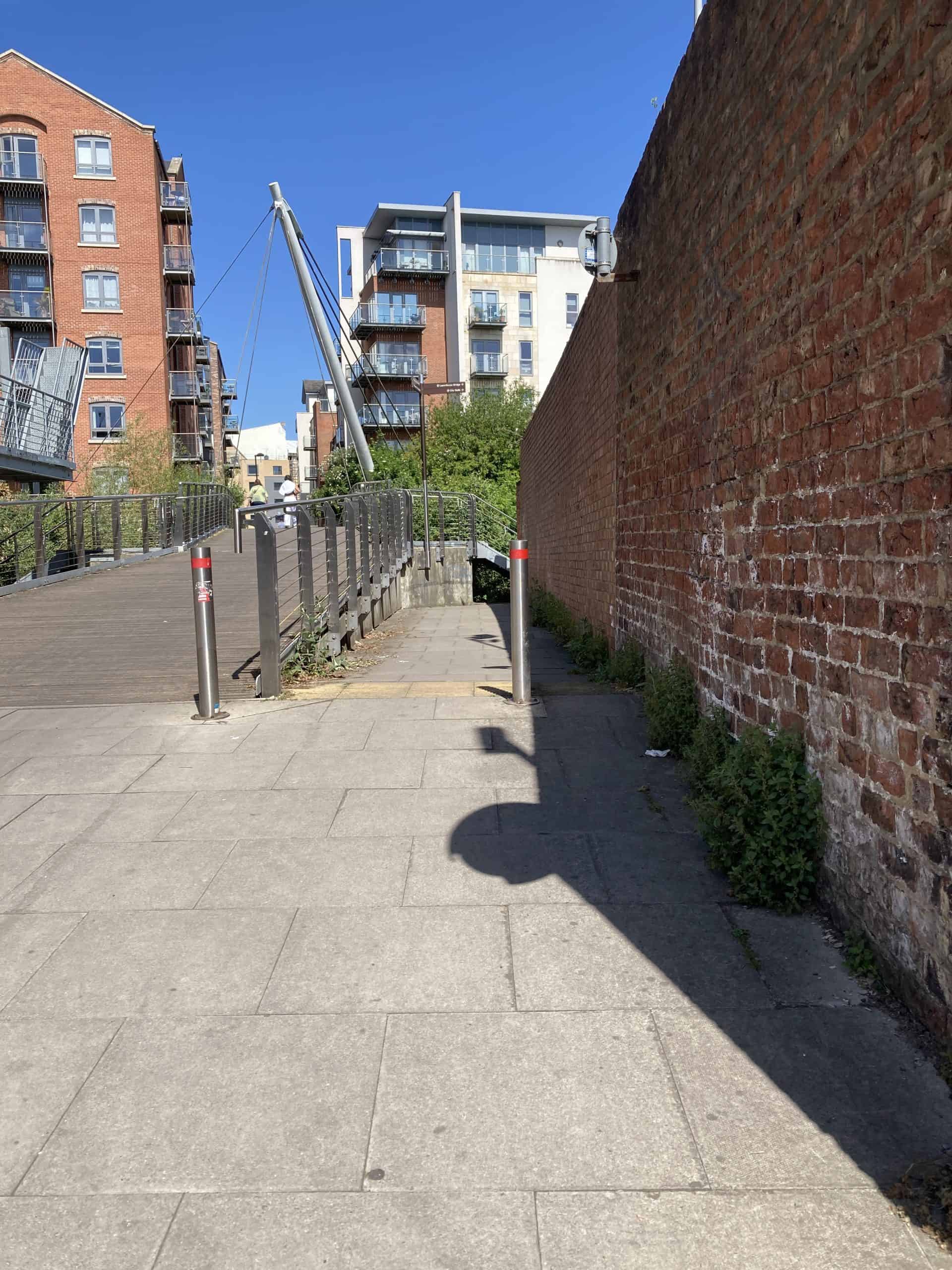 A cycle and pedestrian path which goes up and over a bridge to the left, or down a narrow alley beside a brick wall then around a corner to the right.