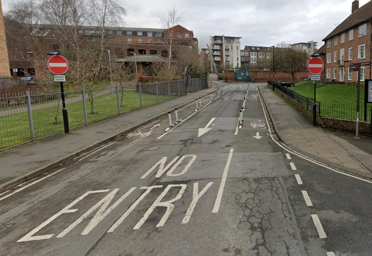 A one-way modal filter with narrow wand-protected cycle tracks on each side of the road. The tactile dropped kerb to the right is unclear about intended crossing direction and has a steep, inaccessible kerb edge.